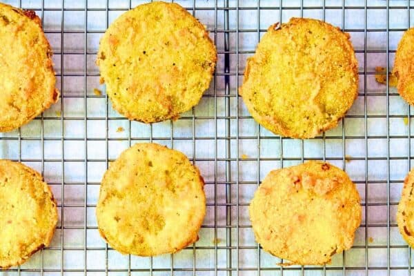 Best Southern Fried Green Tomatoes Recipe - cooked green fried tomatoes draining on a cooling rack on top of white paper towels