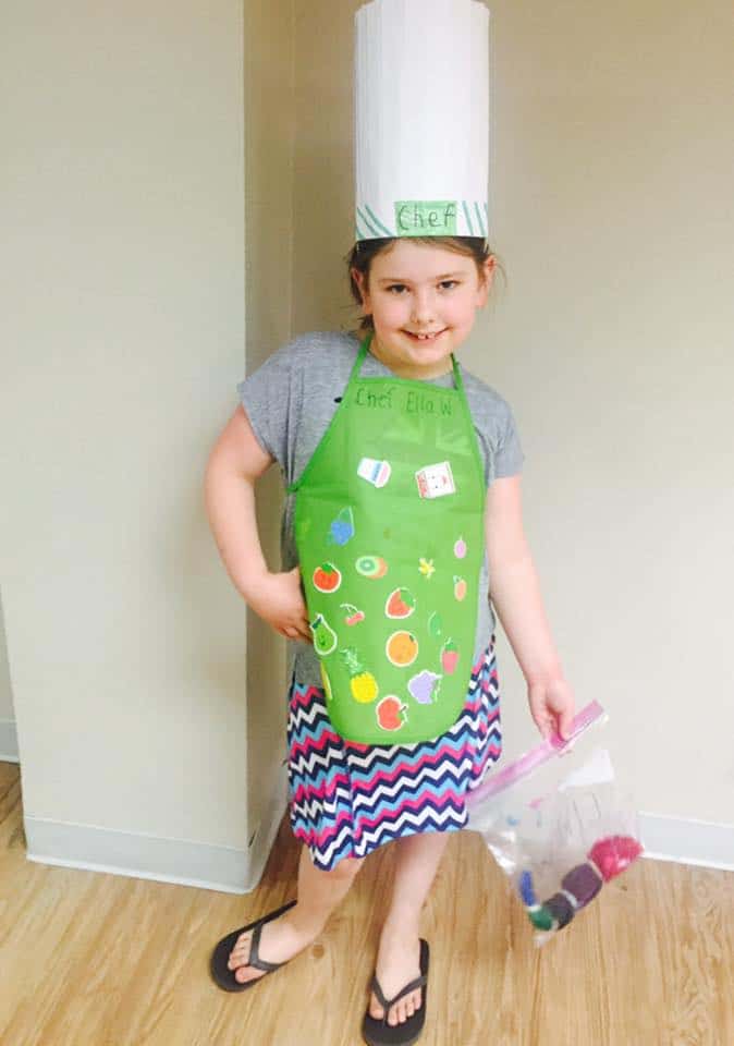 Chef Ella of Little Cooks Reading Books in her chef's hat and a green chef's apron