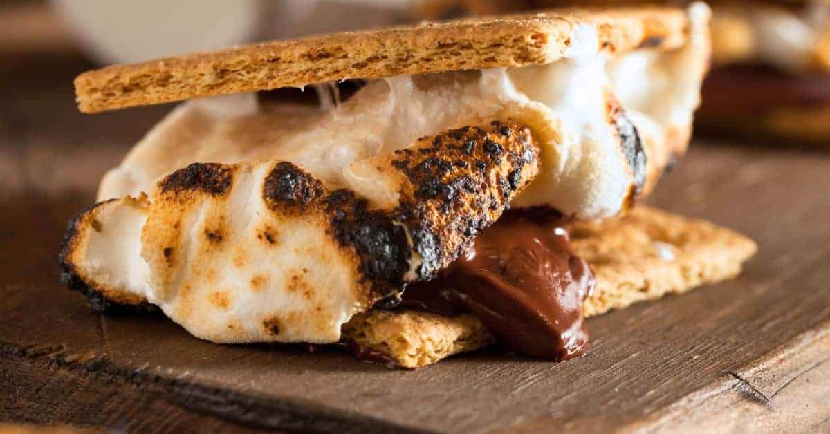 How To Make Traditional Smores - gooey campfire smores with marshmallows, chocolate and graham crackers on a picnic table