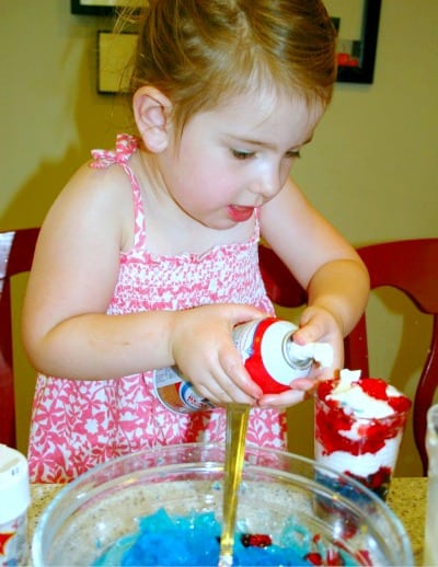 Red White Blue Layered Jello Cups are fun and easy with kids child using canned whipped cream on a red white blue dessert