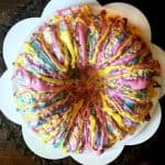 Easy Rice Krispies Cake top view of a round bundt rice krispies cake with different colored bright chocolate drizzled over it on a white plate shaped like a flower