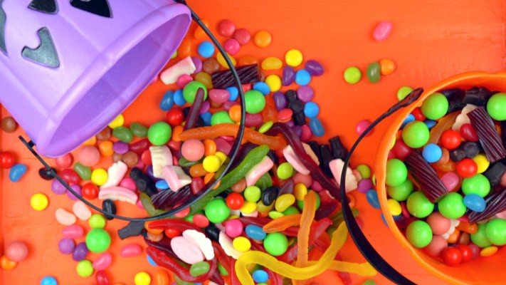 Easy Leftover Halloween Candy Ideas (what to do with extra Halloween candy) with trick or treat Halloween left overs spilling onto a table from a plastic pumpkin