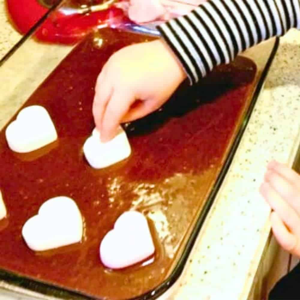 How To Make Valentine's Heart Brownies With Kids child's hands placing heart shaped marshmallows into brownie batter