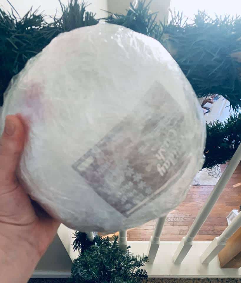 Saran Wrap Ball Game Tips (Plus Secret Ball Wrapping Tip for how to play saran wrap Christmas game!) wrapped plastic ball game in front of Christmas garland