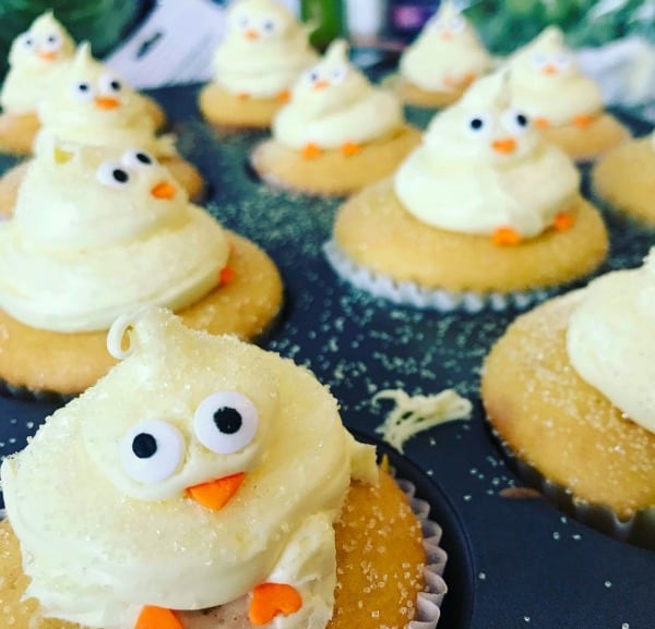 two rows of yellow cupcakes in a cupcake pan with baby chicks made of icing on top