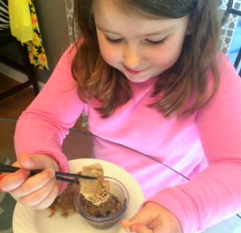 little girl holding a chinese potsticker dumpling with chopsticks over potsticker dipping sauce