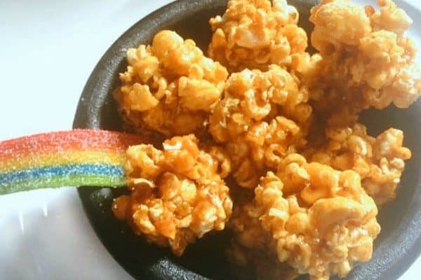 St. Patrick's Day snacks Pot Gold End of Rainbow mini caramel popcorn balls in a black bowl with rainbow candy sticking out of one side