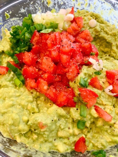 HOW TO MAKE GUACAMOLE STEP BY STEP bowl of mashed guacamole with chopped tomatoes and onions on top