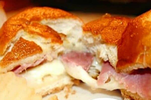 Recipe For Ham And Cheese Sliders with a cheese and ham slider on a plate cut in two halves with melted cheese oozing out