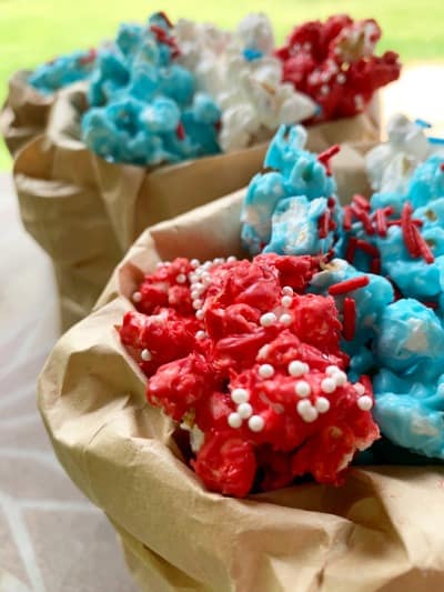 white chocolate covered popcorn in red white and blue colors in a brown paper bag