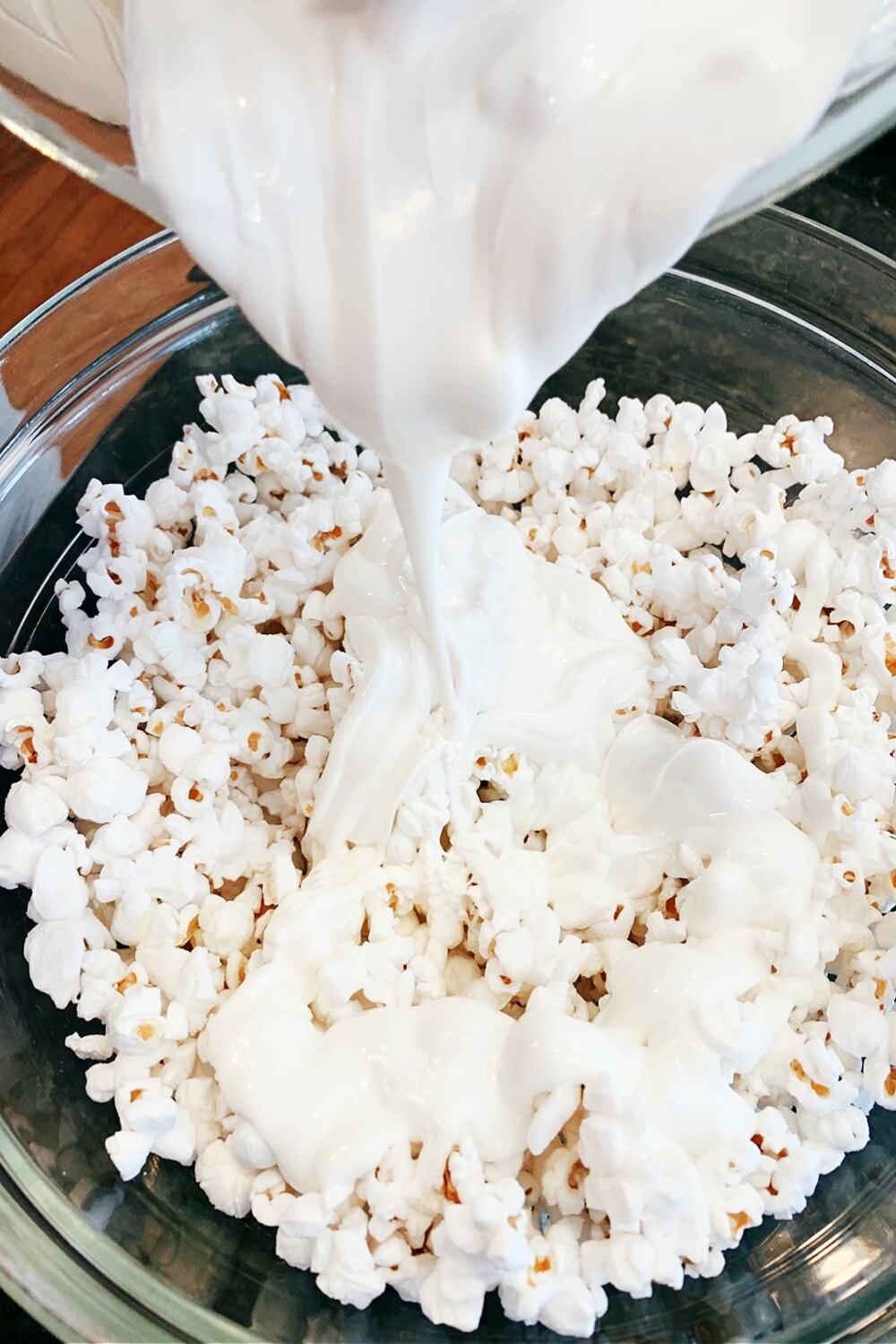 How To Make White Chocolate Covered Popcorn Recipe melted white chocolate poured over white popcorn in a big mixing bowl