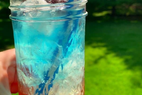 glass held up to the sun with blue white and red layered drink