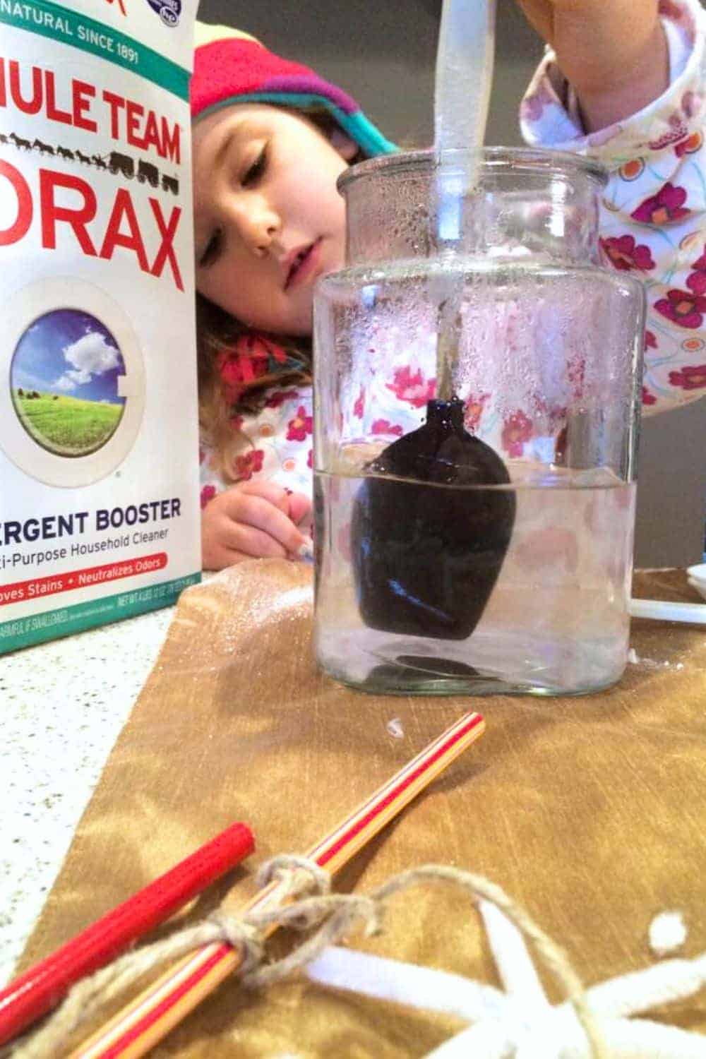 Growing Borax Crystals on Pipe Cleaners (How To Make Borax Crystal Snow Flake) - young child stirring Borax detergent in large jar for crystal craft