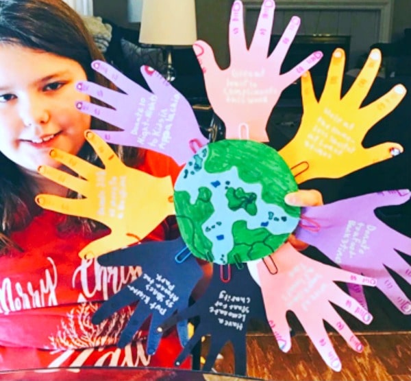 child with a helping hands craft of different colored cutout hand tracings attached to a world drawing