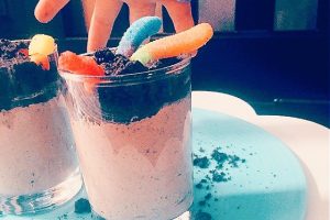 Dirt Pudding With Oreos cups with a small child's hand reaching down for a gummy worm