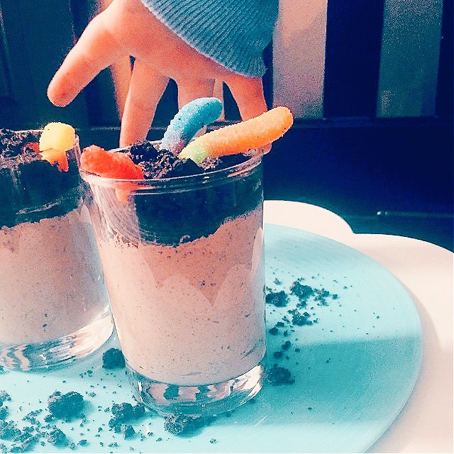 Dirt pudding cups with a small child's hand reaching down for a gummy worm