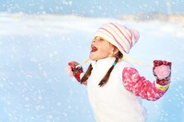 Snow Activities: young girl in winter hat and vest catching snowflakes on her tongue