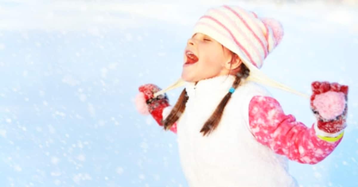 Snow Activity Ideas with young girl in a winter hat outdoors in snow and catching snowflakes in her mouth