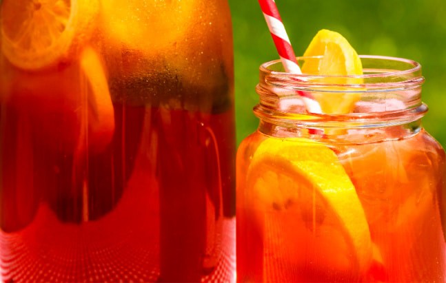 Sun Tea with full glass tea jar and sun tea in a mason jar with colorful straw sitting on picnic table on a summer day