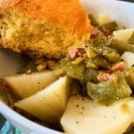 green beans and potatoes in a white bowl with a piece of cornbread sitting on the side