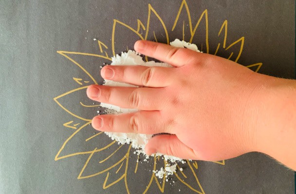 child's hand on black paper doing a Pollinator Craft for kids