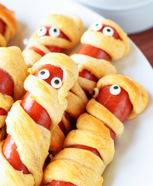 Mummy Hot Dogs For Halloween stacked on a white plate