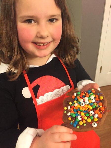 How To Host A Christmas Cookie Exchange Party little girl holding up a decorated christmas cookie with lots of candy