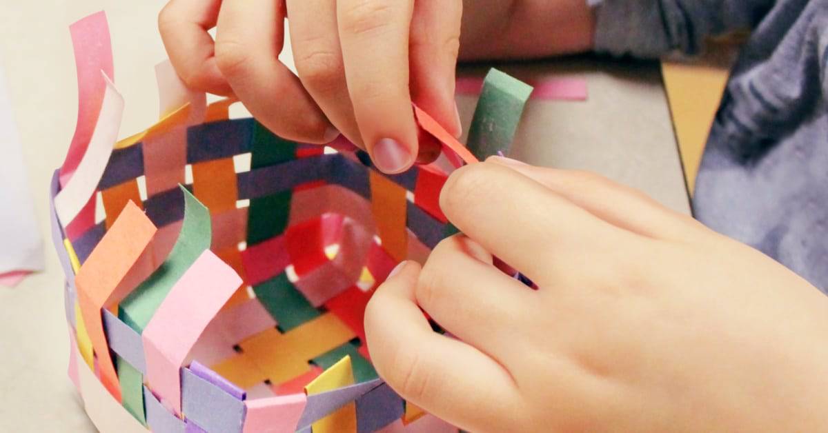 Crafts for Native American Heritage Month young child's hand weaving a paper basket of bright colors