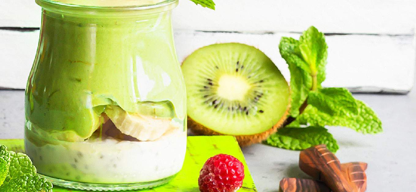 St Patricks Day Pudding Parfait on a table with kiwi, raspberry and mint leaves around it