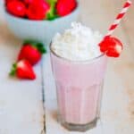Homemade Pink milkshake with whipped cream on a table with a bowl of strawberries