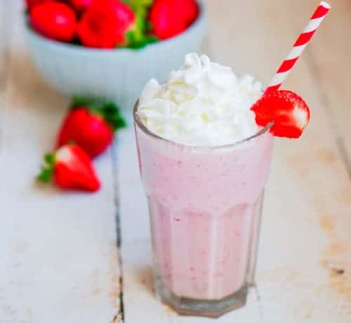 Homemade Pink milkshake with whipped cream on a table with a bowl of strawberries