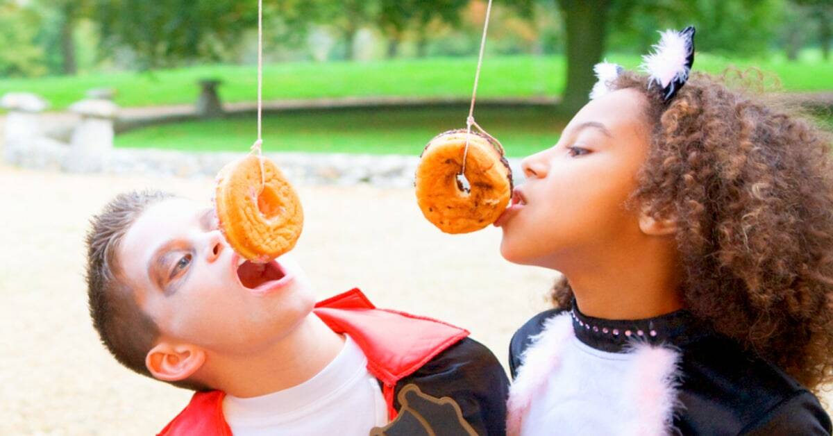 Halloween Donut Hanging Game girl and boy playing the doughnut on a string game dressed in Halloween costumes