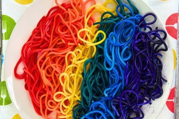 Colored Spaghetti Recipe For Kids on a white plate and a dishtowel with colored forks