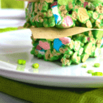 Green Lucky Charm Rice Krispies Treats stacked on a white plate in front of a window