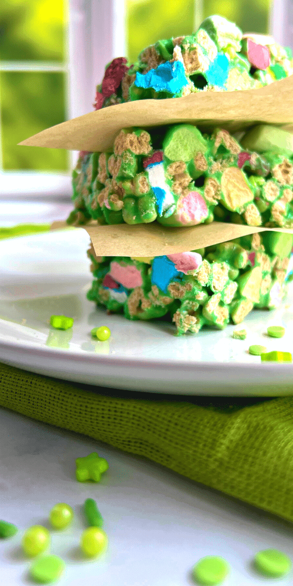 Green Lucky Charm Rice Krispies Treats stacked on a white plate in front of a window