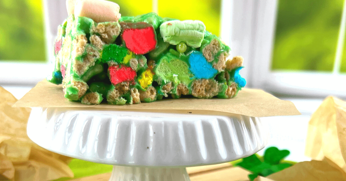 Lucky Charms St Patrick’s Day Rice Krispies Treats (Green lucky charm treats!) on a white plate in front of a window