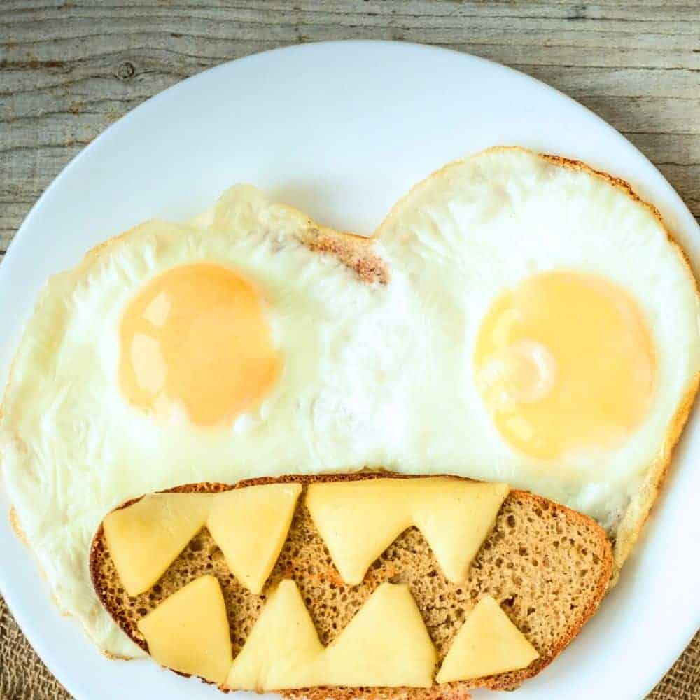 Breakfast Halloween Monster Eggs and Toast 2 over easy eggs that look like eyes with Halloween toast under them and cheese cut to look like sharp monster teeth on top of toast
