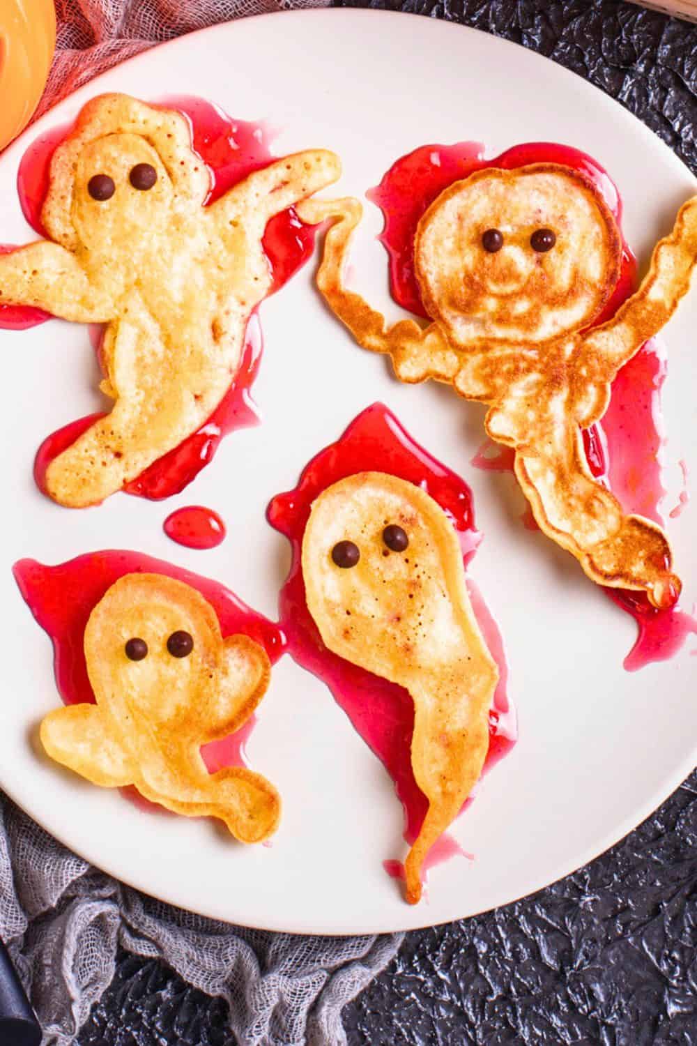 Spooky Breakfast Bites (Spooky Halloween Pancakes) - Halloween ghost pancakes on top of strawberry syrup