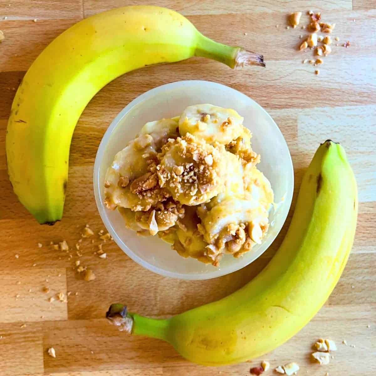 Simple Banana Peanut Salad Recipe From The South top down view of peanut banana salad desserts in a dessert dish with fresh bananas and crush peanuts around it on a table
