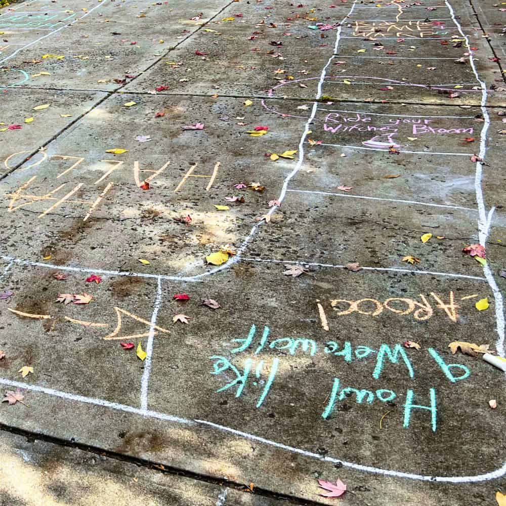 FUN HALLOWEEN ACTIVITY FOR KIDS HALLOWEEN TRICK OR TREAT TRAIL GAME chalk Halloween hopscotch blocks game drawn on a driveway with fall leaves blowing on it