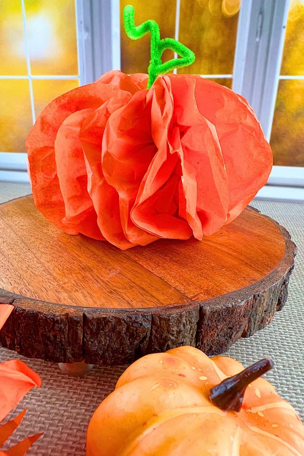 DIY Pumpkin Tissue Paper Craft Idea finished orange paper pumpkin on a table in front of a fall window