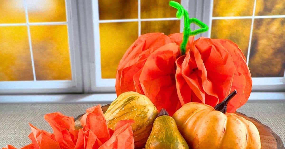 DIY Tissue Paper Pumpkin Craft pumpkin made of tissue paper sitting on a table in front a window with fall leaves in the background