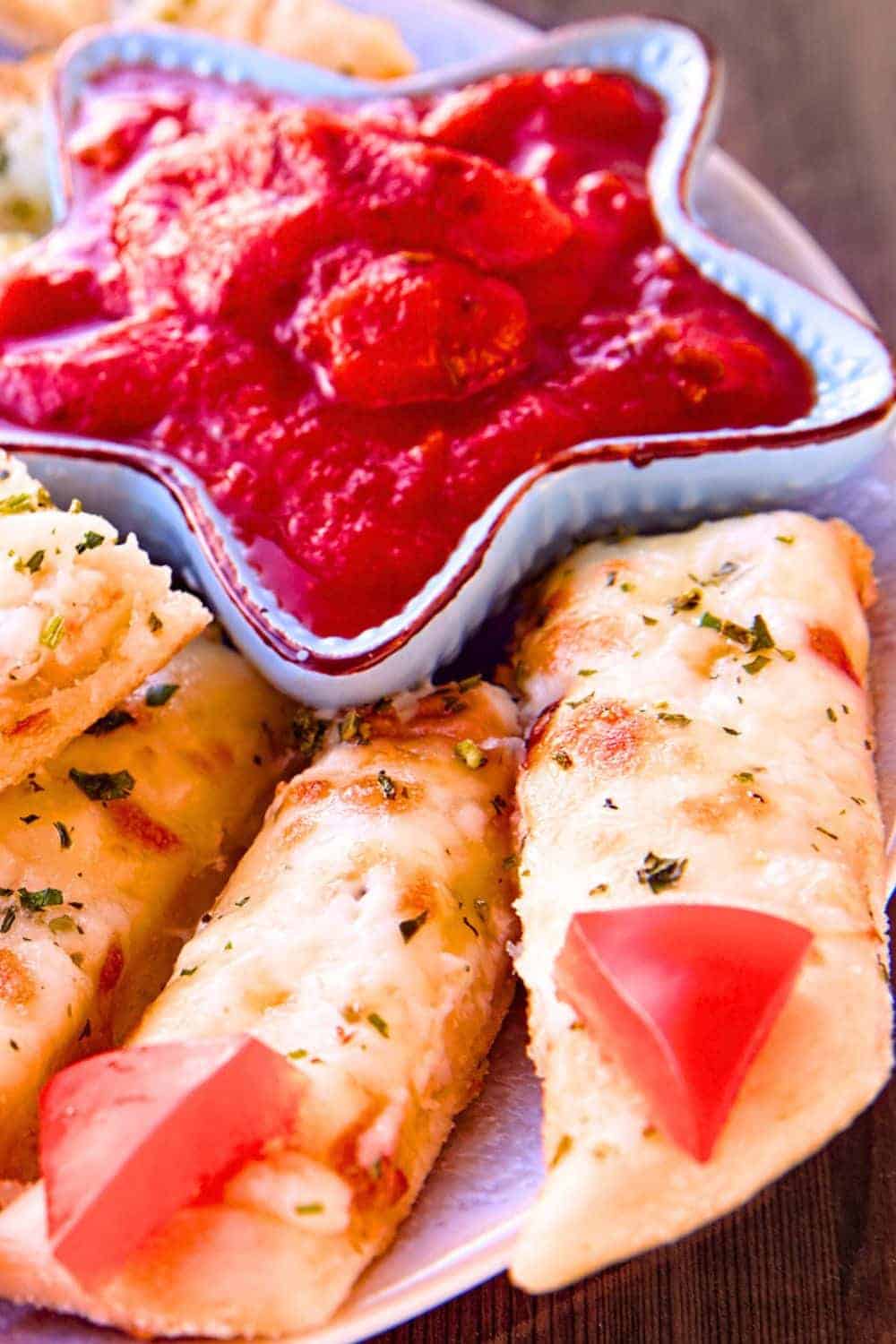 Zombie Food Pizza Fingers (Zombie Party Recipes) - pizza sticks that look like zombie fingers with a side of marinara sauce on a plate