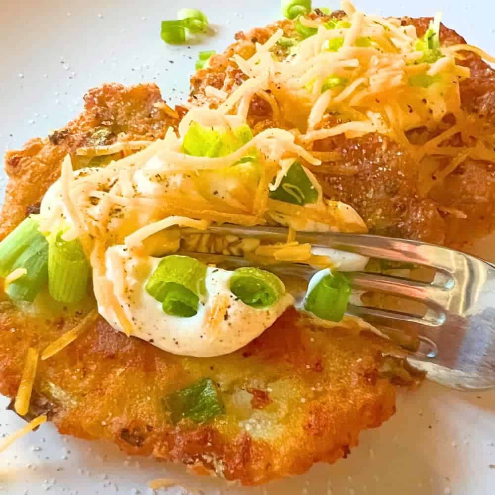 Best Leftover Mashed Potato Pancakes Recipe - fork cutting into potato cake with toppings on a white plate