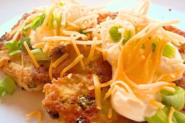 Old Fashioned Leftover Mashed Potato Cakes with toppings of cheese, onions, and sour cream on a white plate