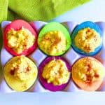 Easy Colored Deviled Eggs Dyed Egg Whites - eggs white dyed bright colors with deviled egg filling in an egg holder on a white counter with a green napkin