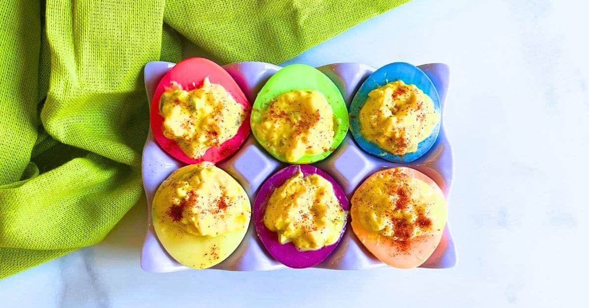 Easy Colored Deviled Eggs Dyed Egg Whites - eggs white dyed bright colors with deviled egg filling in an egg holder on a white counter with a green napkin