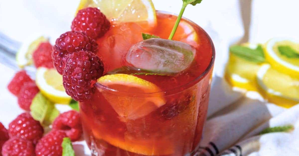 Lemon Sparkling Raspberry Punch Recipe in a glass on a table with fresh raspberries and fresh lemons around it