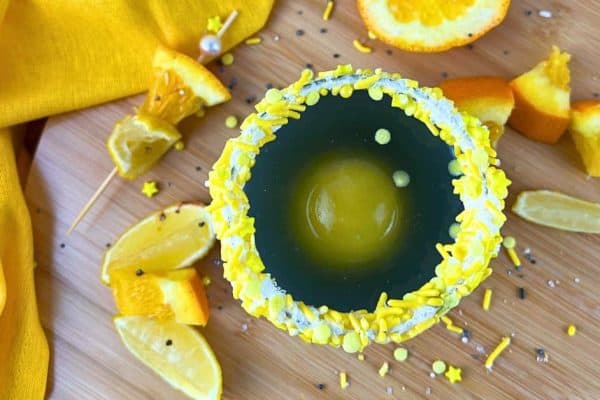 Solar Splash Eclipse Party Punch Drink For Kids - black punch with a round orange juice ice cube in a glass with a yellow sprinkles rim