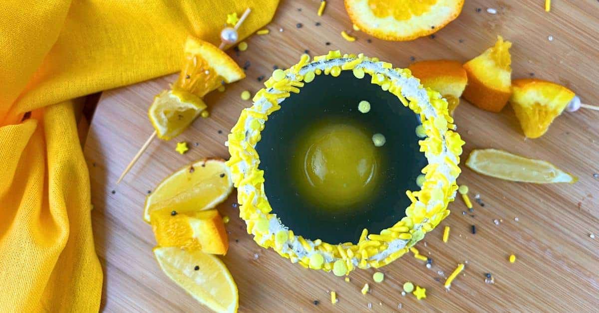 Solar Splash Eclipse Party Punch Drink For Kids Fun For Eclipse Parties - black punch with a round orange juice ice cube in a glass with a yellow sprinkles rim